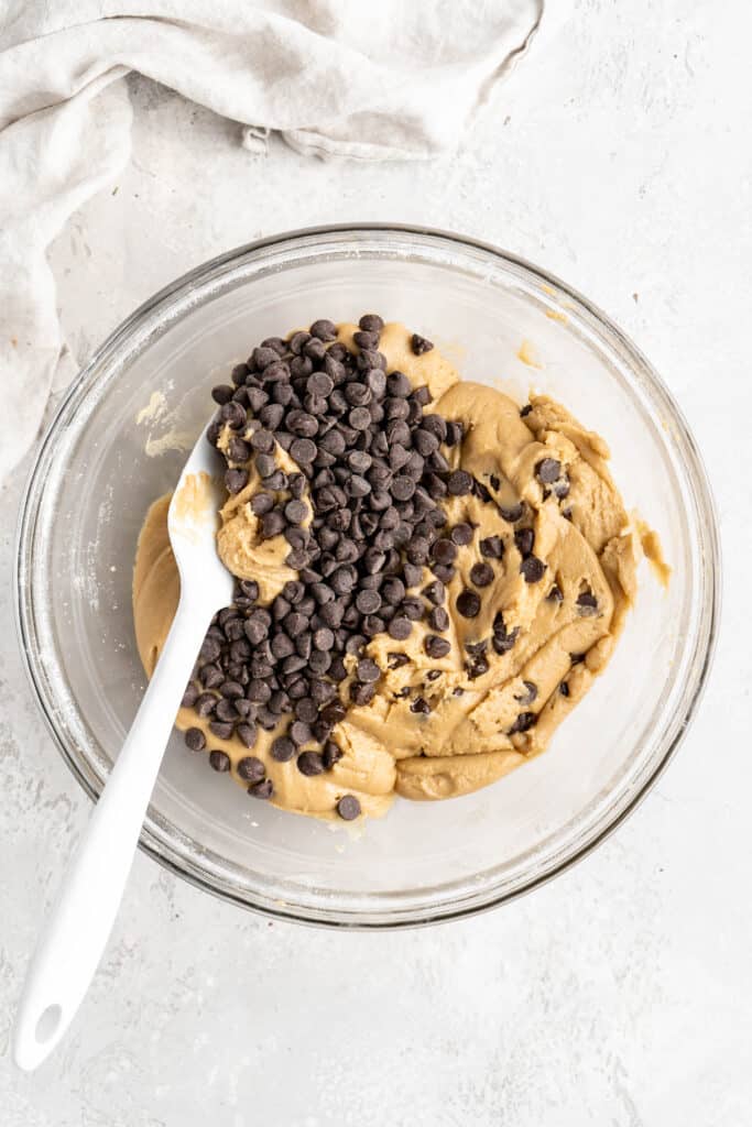Cookie dough being folded together with a spatula and chocolate chips