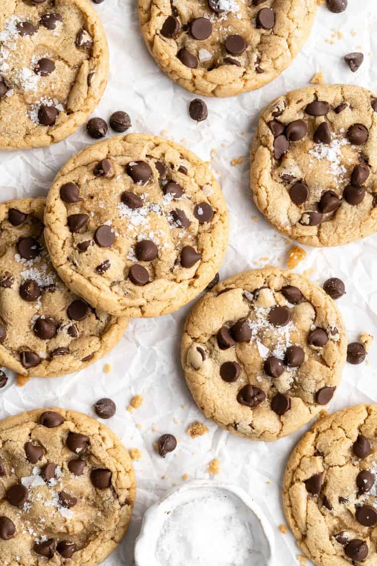 A close up of brown butter chocolate chip cookies scattered on a white background