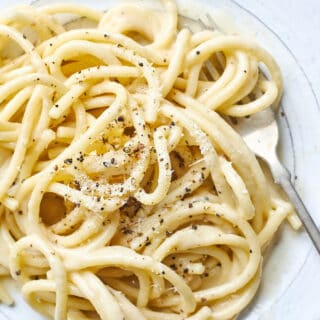 A close up of cacio e pepe on a white plate with a fork