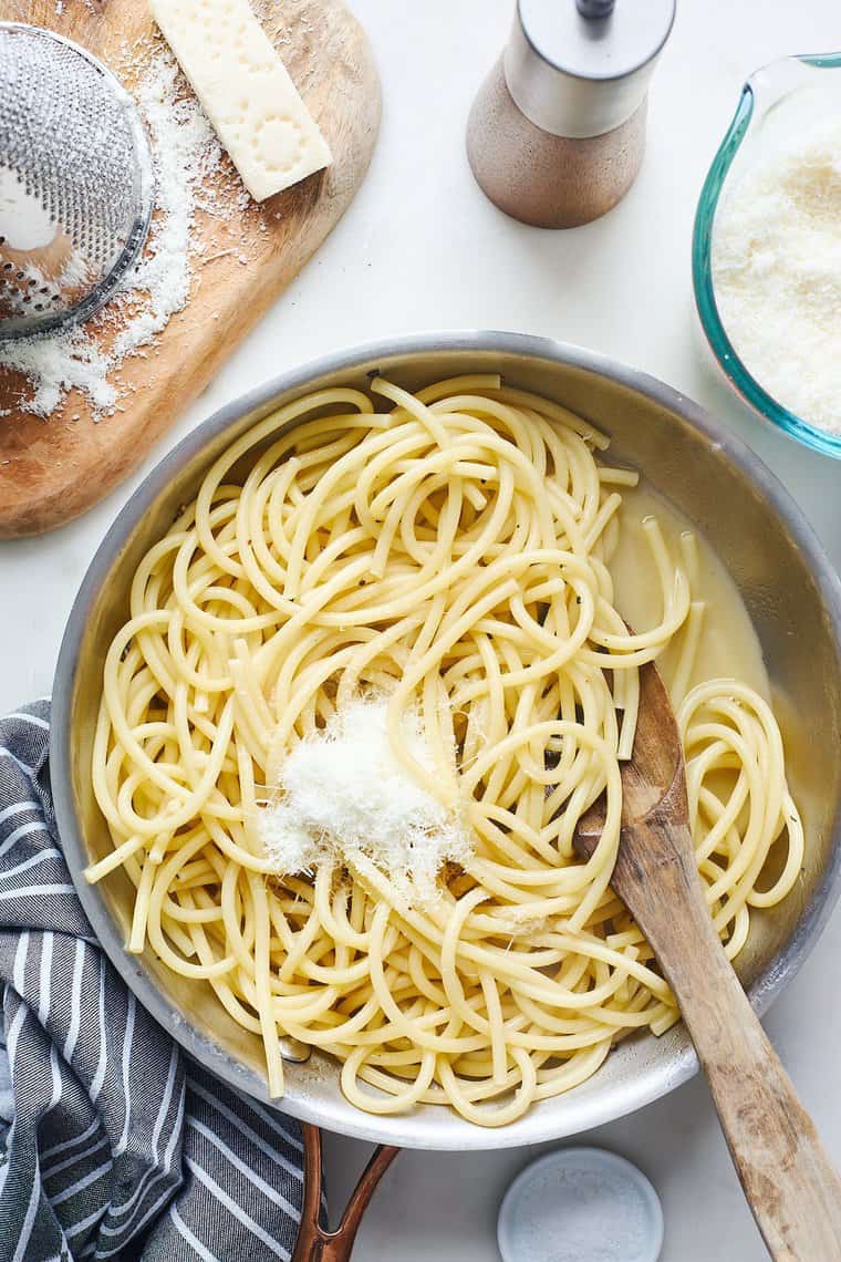 Pasta in a skillet with parmesan being stirred into the pot