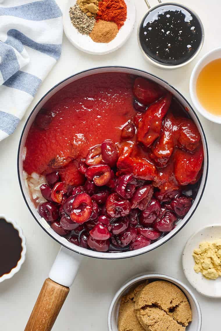 Pitted cherries being stirred together with tomato past in a large pot