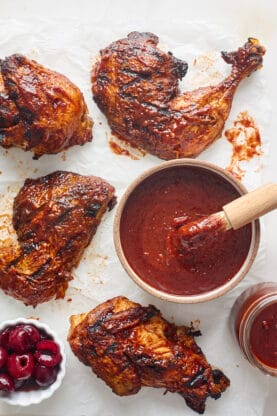 A brush of barbecue sauce being added to a big bowl of it with bbq chicken surrounding it