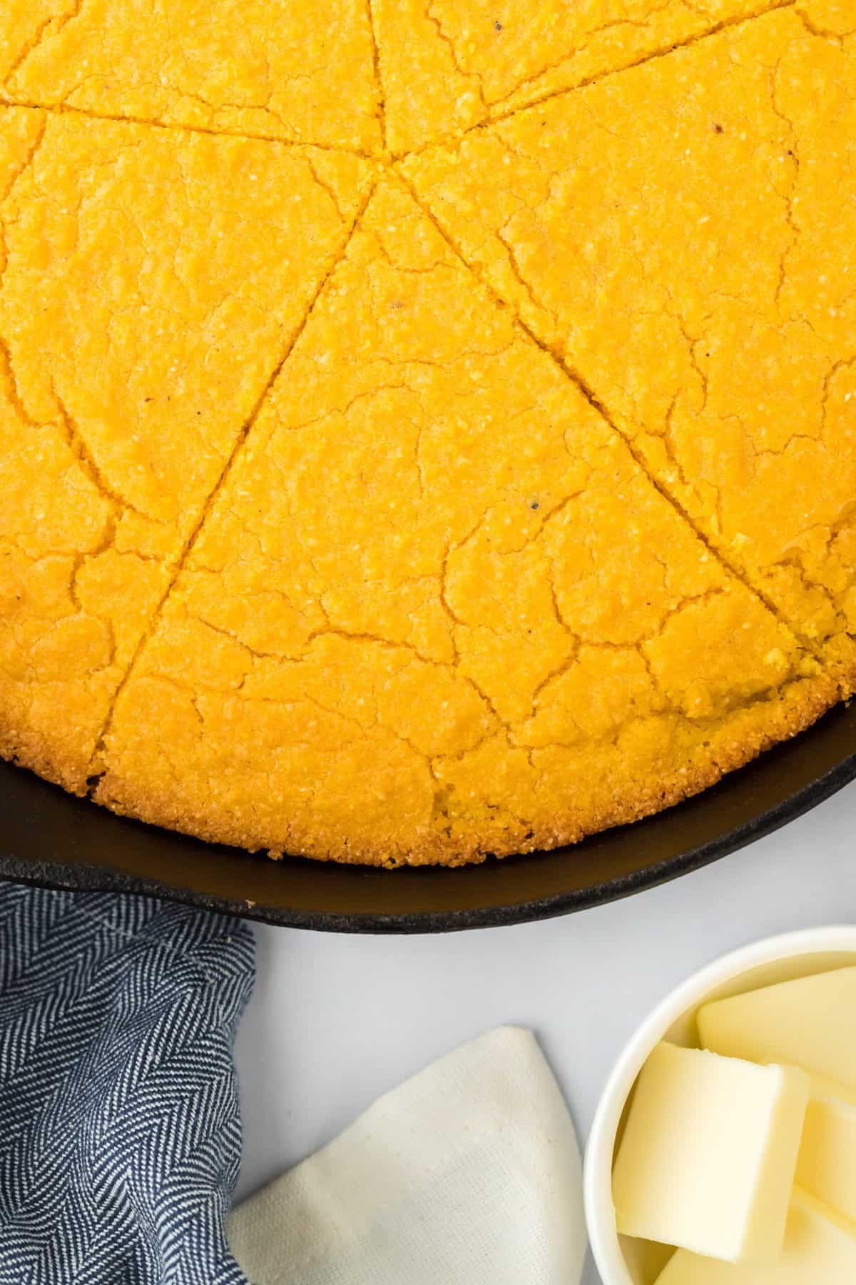 Sliced corn pone recipe overhead in a cast iron skillet with butter nearby