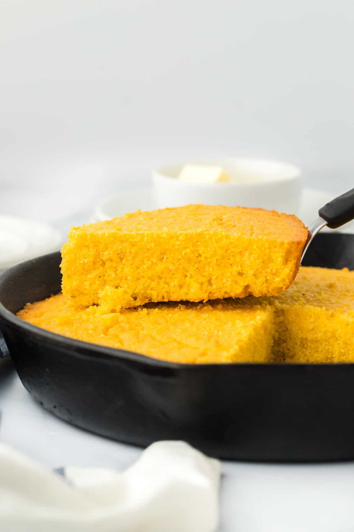 Slices of corn pone coming out of a cast iron skillet in a white background