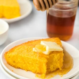 A slice of eaten corn pone recipe on a white plate with butter and honey drizzle