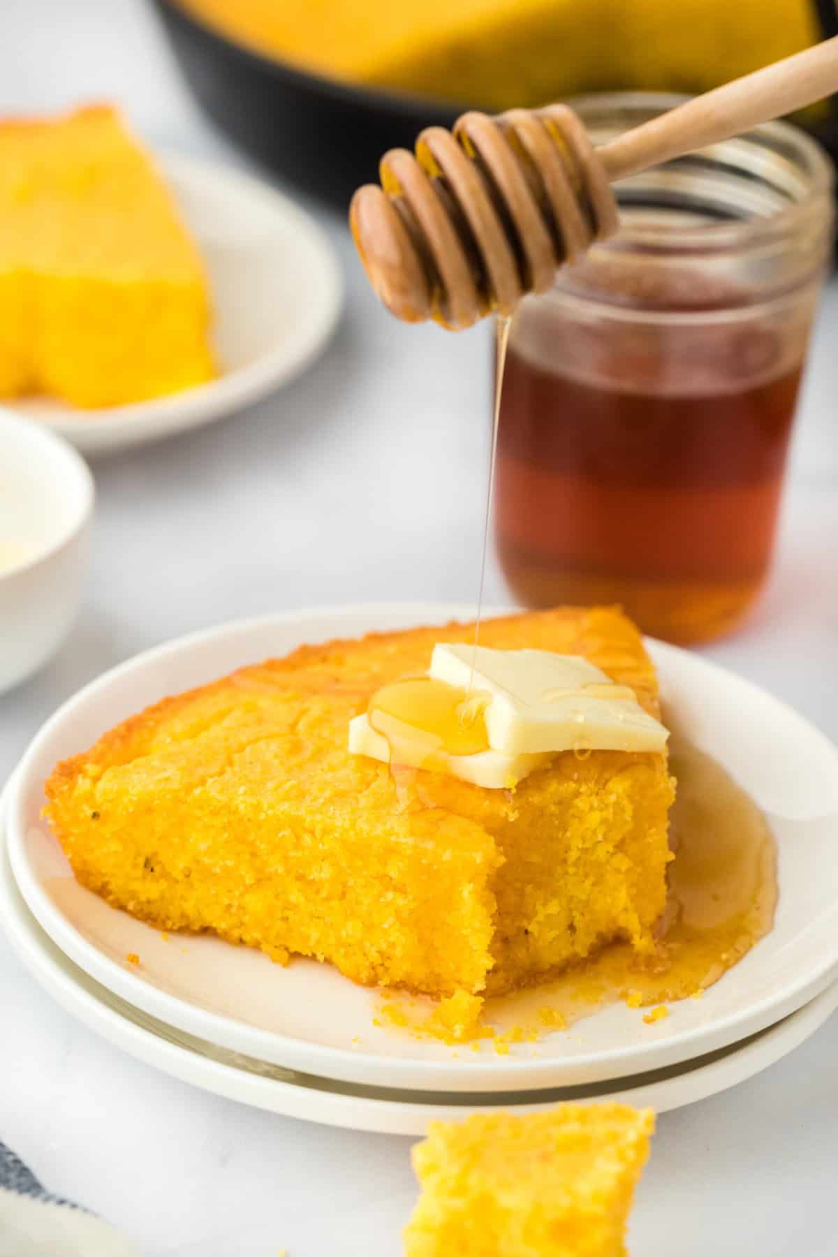 A slice of eaten corn pone recipe on a white plate with butter and honey drizzle