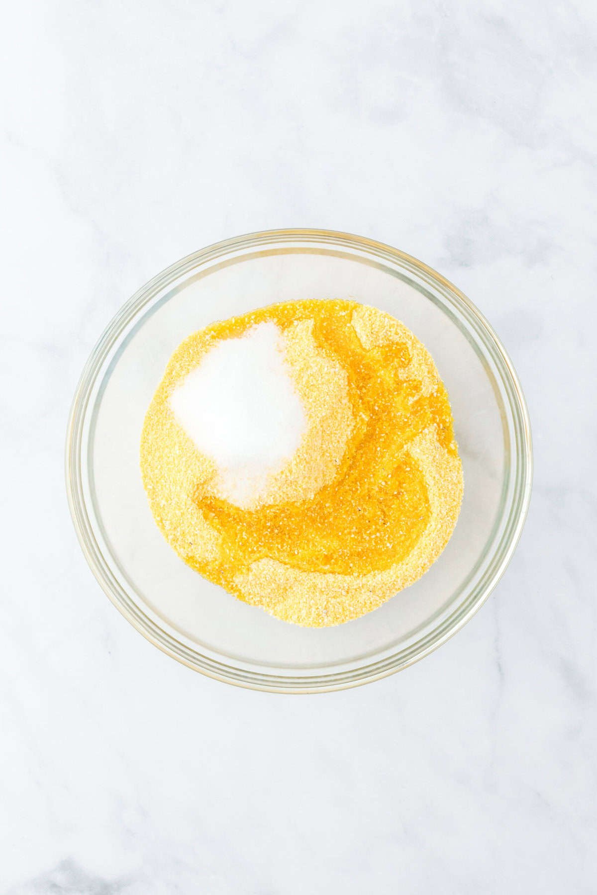 Cornmeal, salt and bacon fat added to a clear bowl on a white background