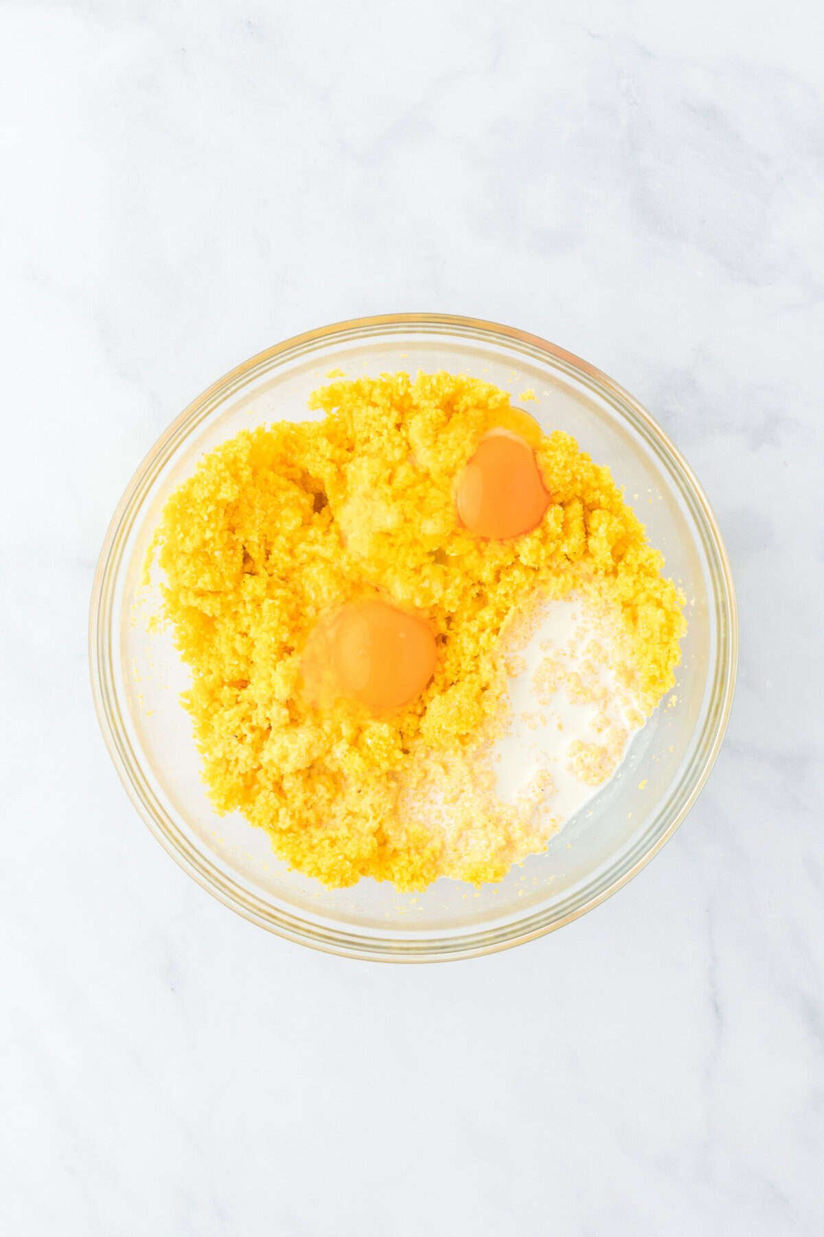 Eggs, cream and baking powder added to a clear bowl with corn pone mixture