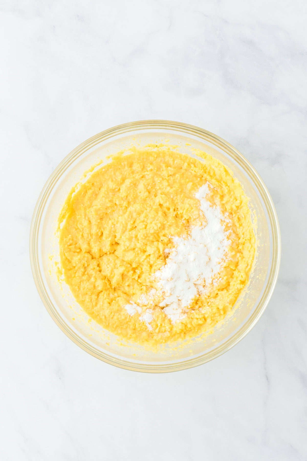 Baking powder added to cornmeal mixture in a clear bowl on a white background