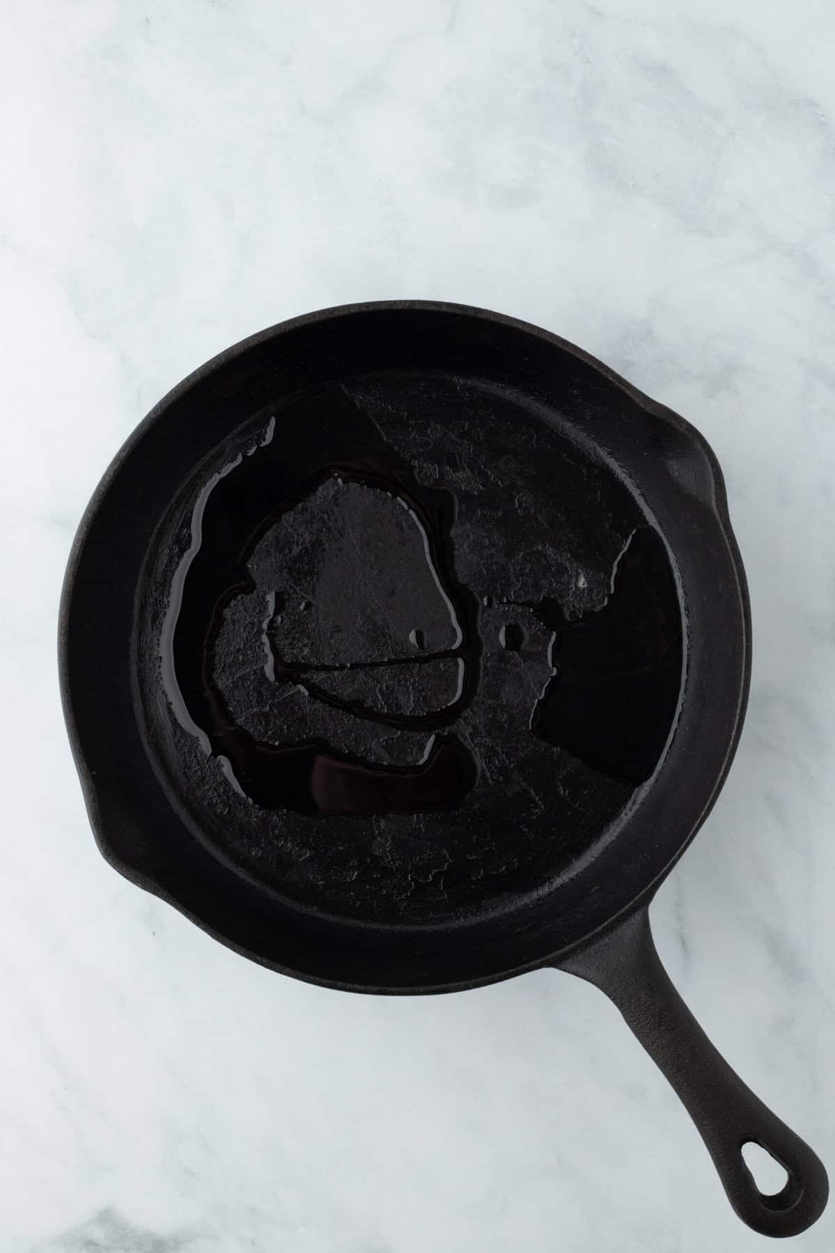 A cast iron skillet with oil added on white background