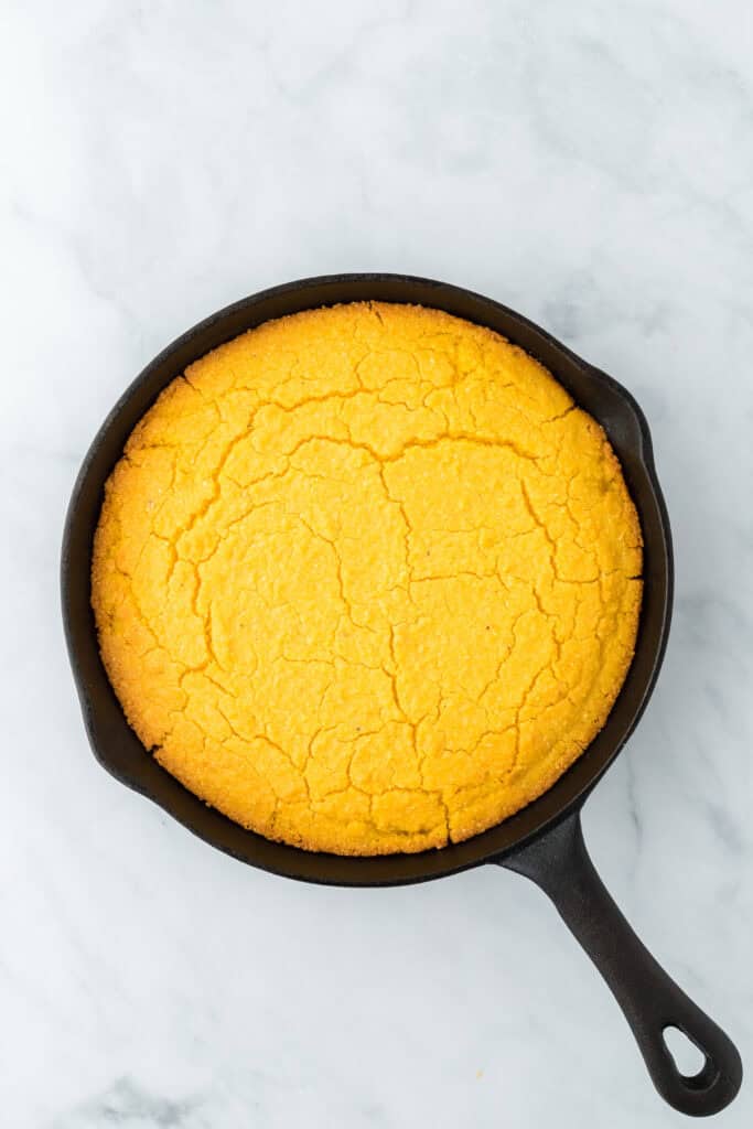 Baked corn pone in a cast iron skillet on a white background