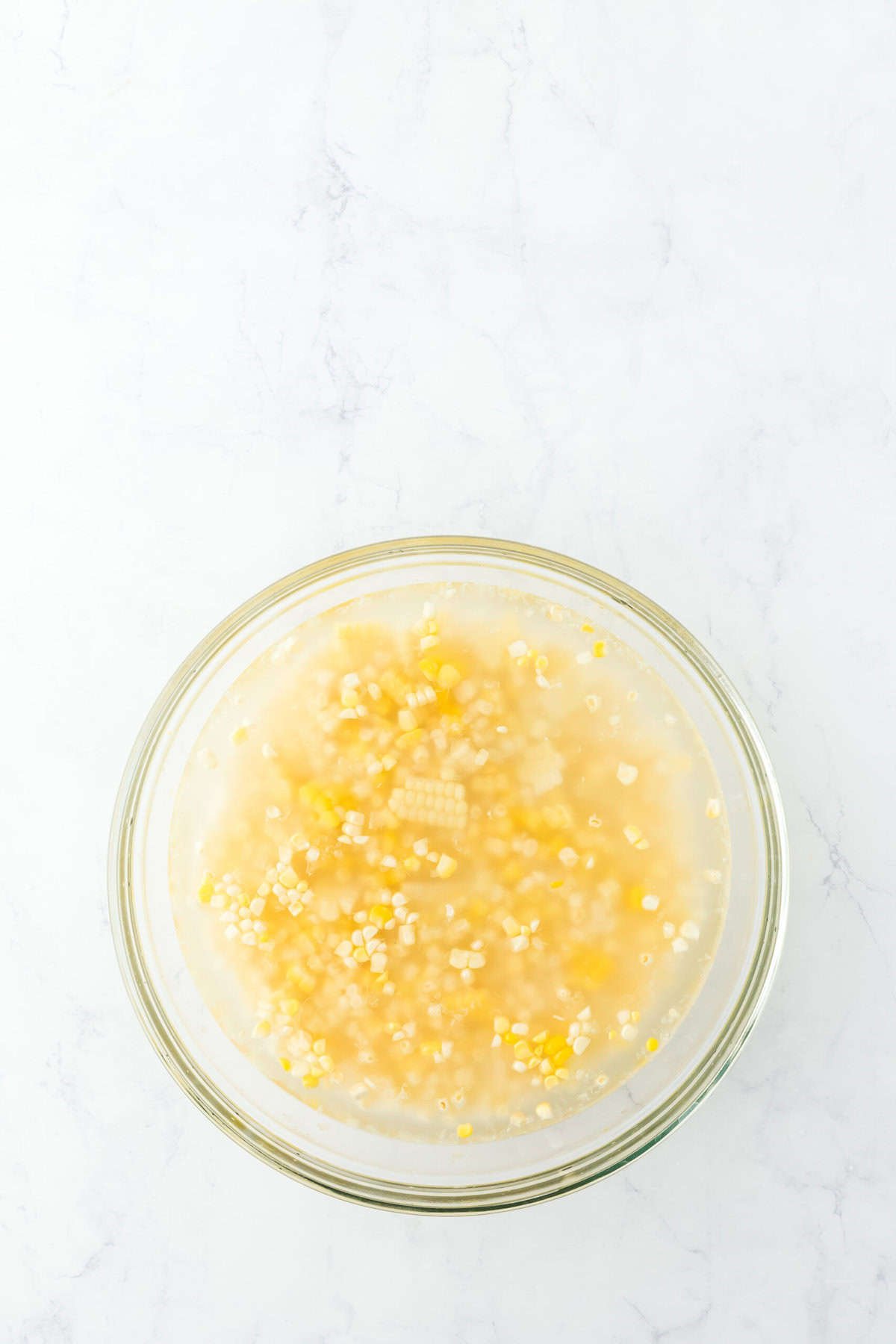 Cut corn kernels added to a glass bowl with water on white background