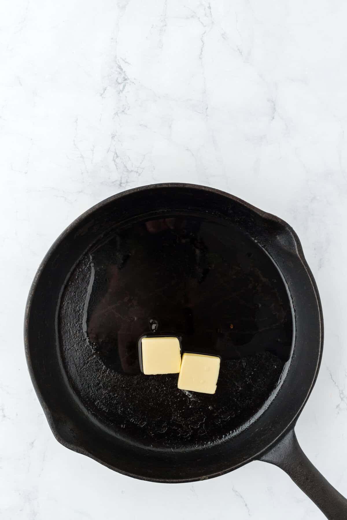 Butter pats and bacon grease in a cast iron skillet to white background