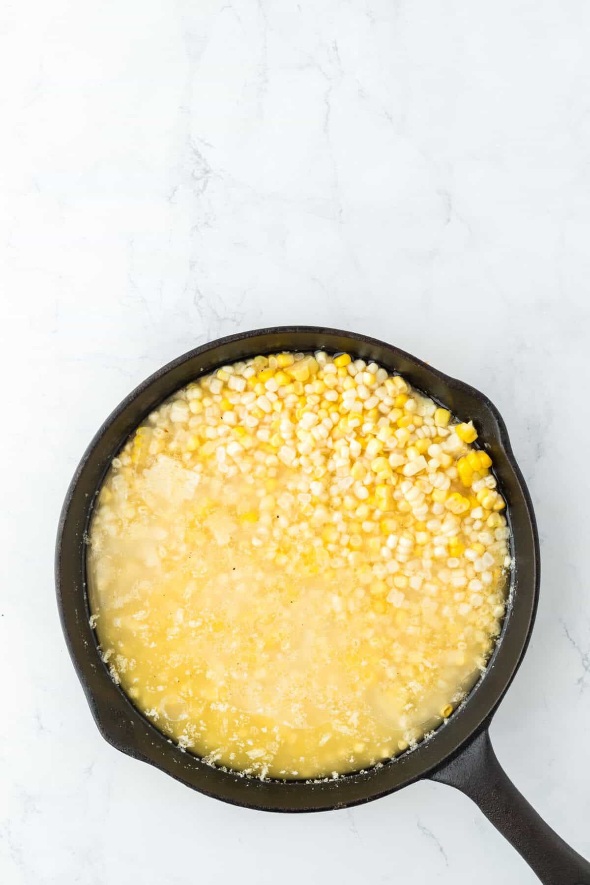 Water and corn added to a cast iron skillet on a white background