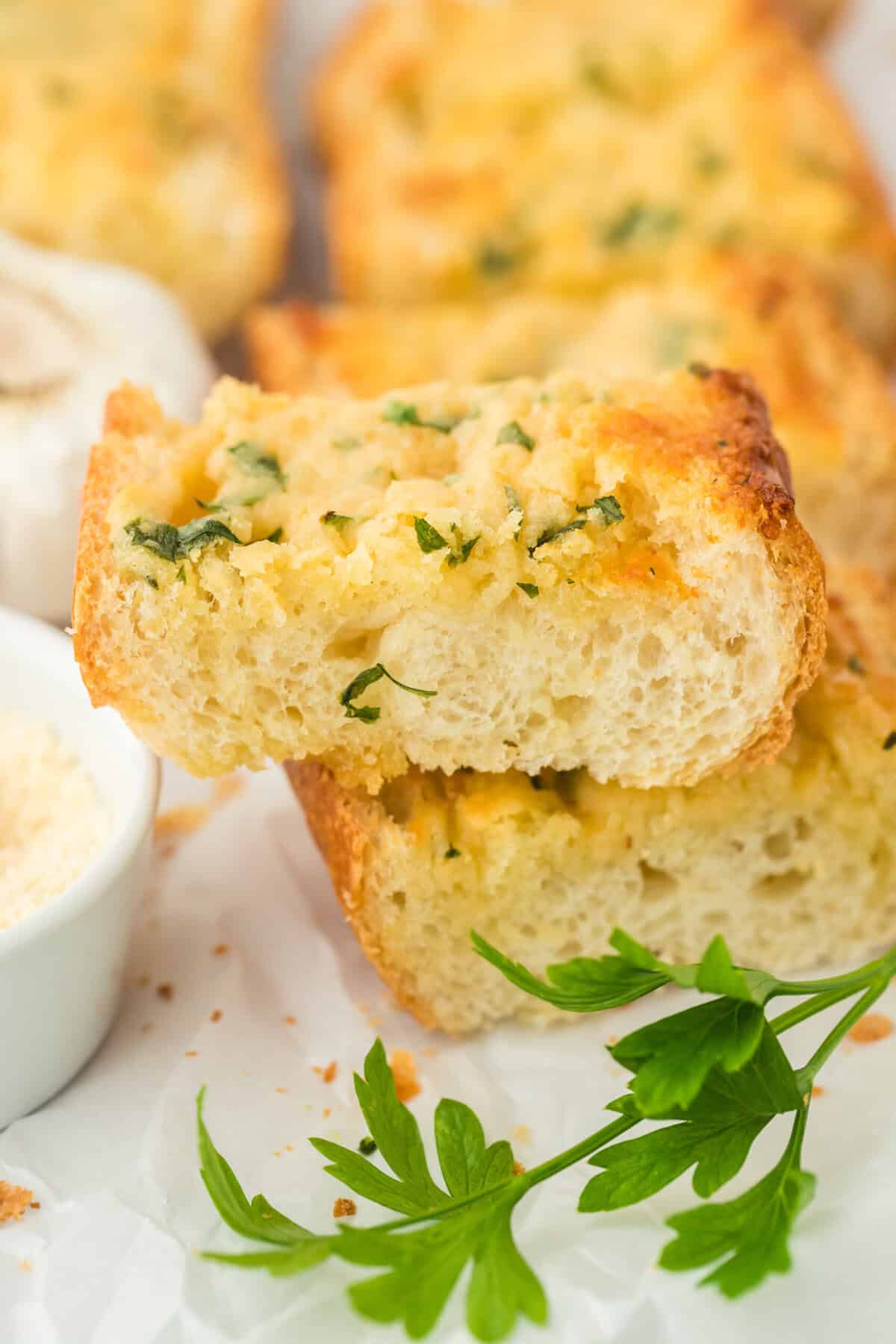A close up of the inside of garlic bread from scratch on a white plate with parsley in front of it