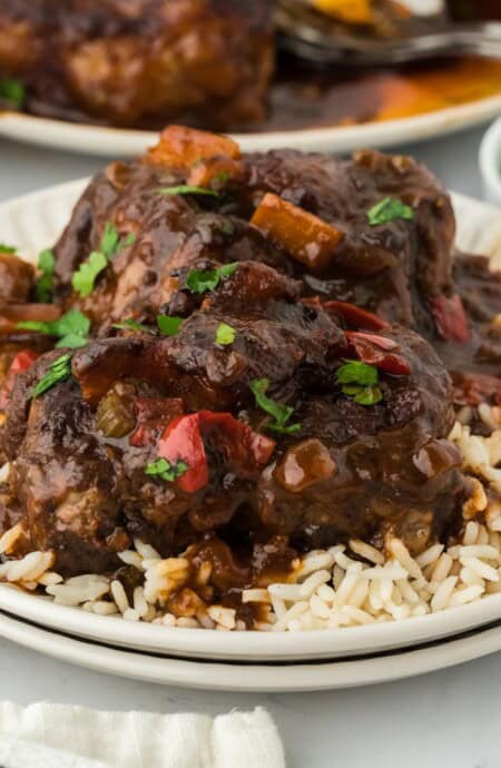 Close up of Jamaican oxtail stew served over rice, showing tender oxtail pieces and rich gravy with red bell peppers