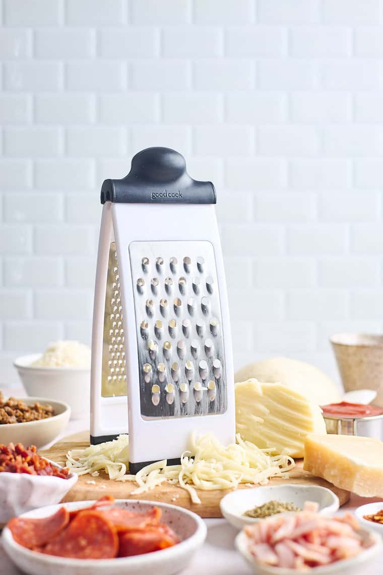 Cheese shredder and pizza ingredients against a white background