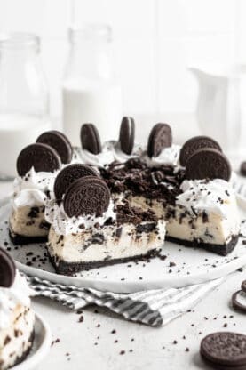 A slice of oreo cheesecake against a full cake in a white background