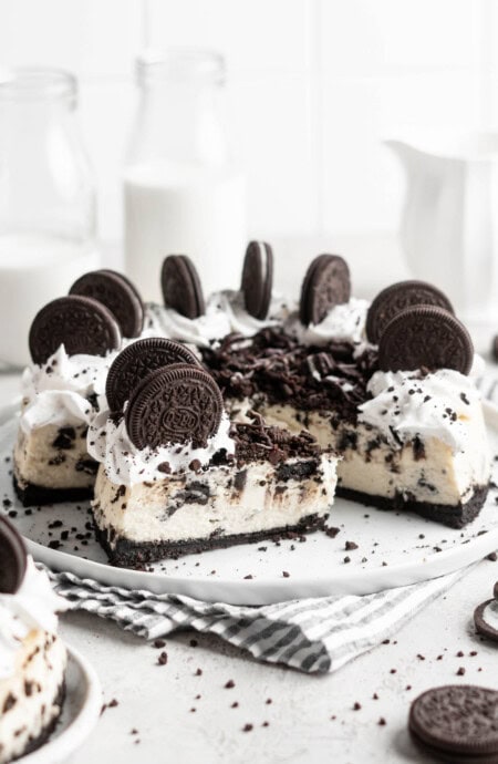 A slice of oreo cheesecake against a full cake in a white background