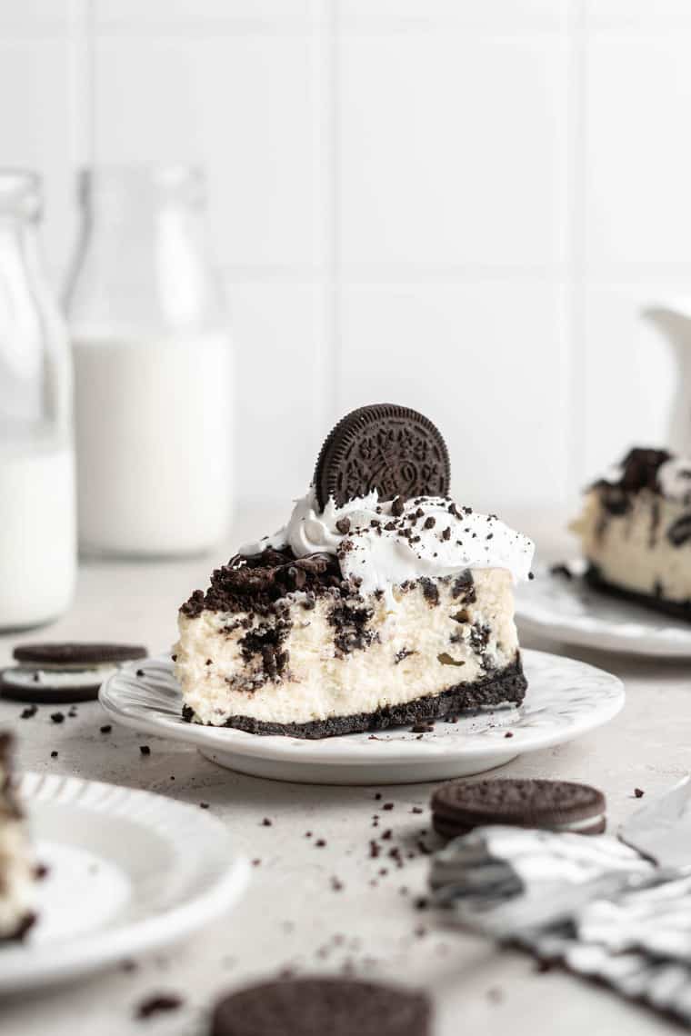 A slice of cookies and cream cheesecake on a white plate with milk in the background