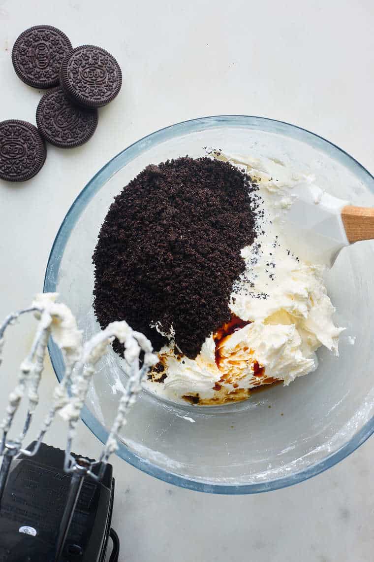 Oreo frosting being mixed together in a glass bowl with a hand mixer