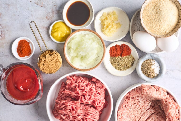 Ground pork, beef, spices, brown sugar, ketchup all in white bowls against a gray background