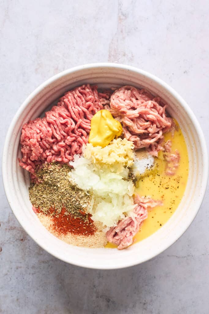 Ground meat, onion, spices in a large white bowl before mixing together