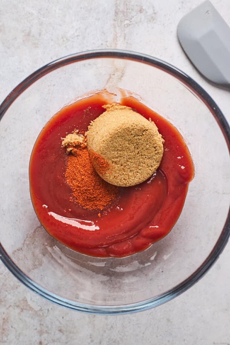 Ketchup, brown sugar and cayenne in a clear bowl before mixing together