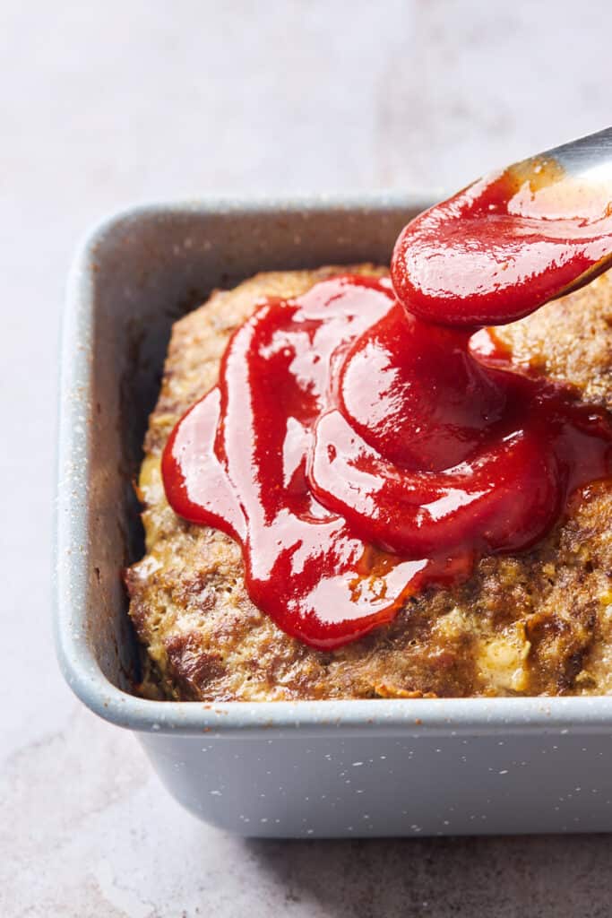 Sauce being poured on top of perfect meatloaf recipe before finishing in the oven