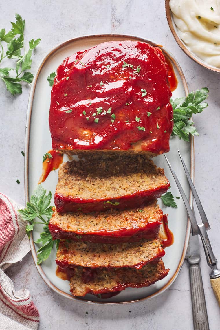 A perfect meatloaf recipe on a white serving platter with slices cut to serve