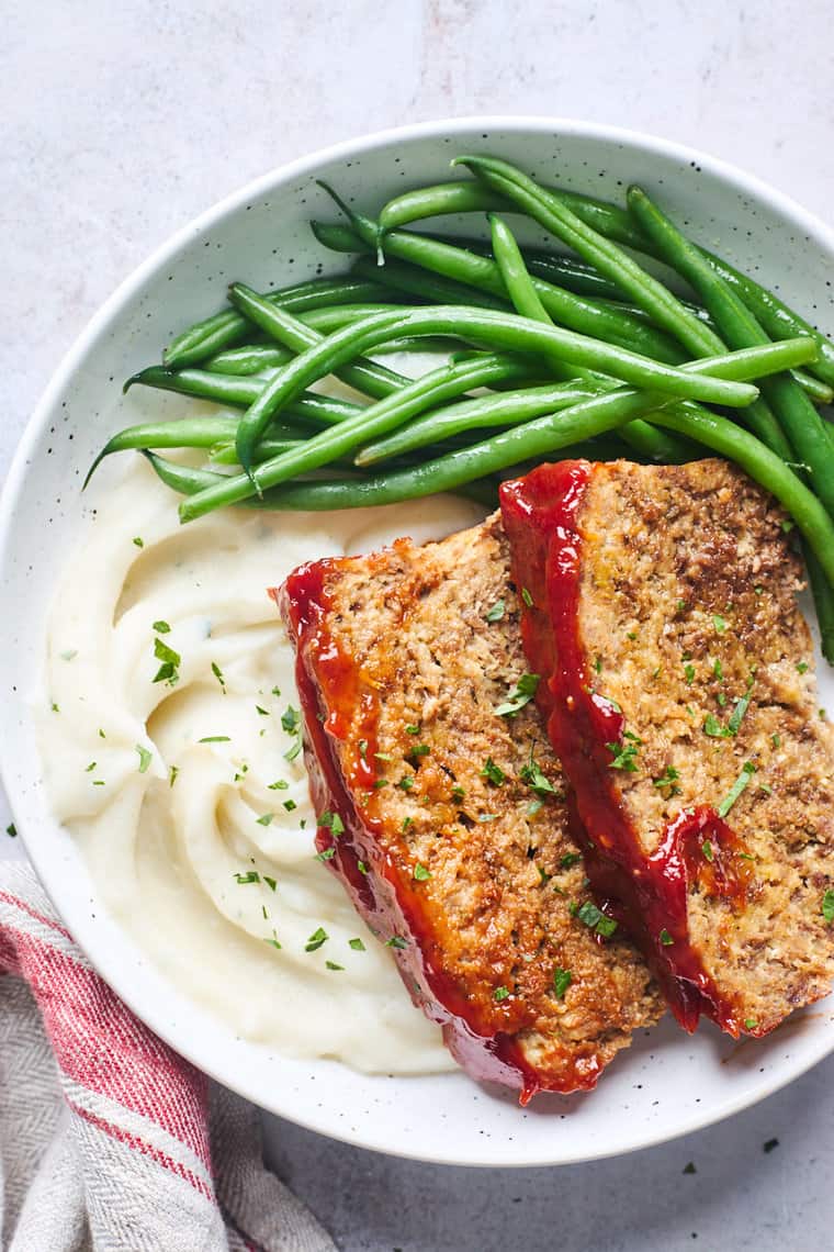 Slices of perfect meatloaf on a plate with mashed potatoes and green beans