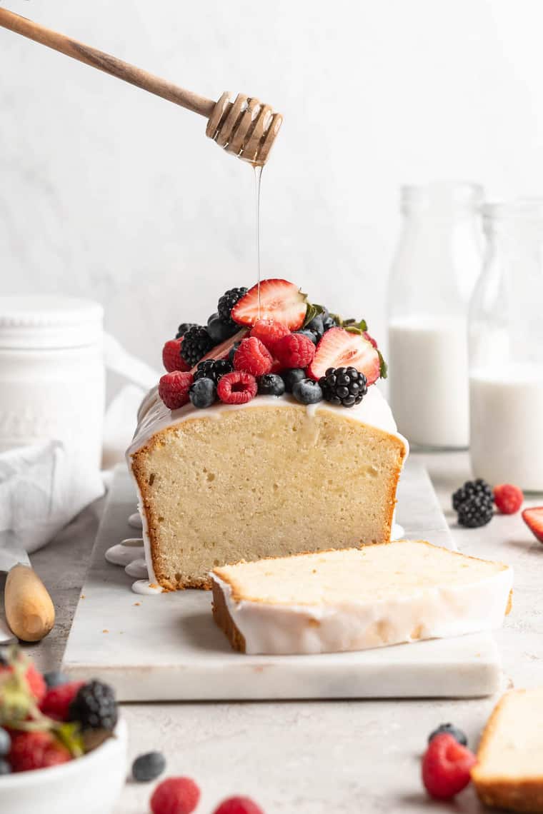 Honey being drizzled on top of a sour cream cake with assorted berries osn top