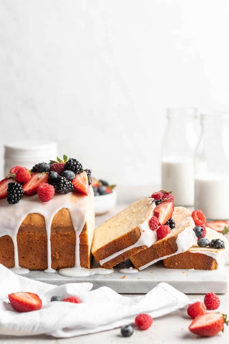 A loaf pound cake with three slices cut and berries on top with a white background