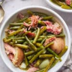 Two bowls of Southern style green beans with potatoes in them with ham hock on a white background