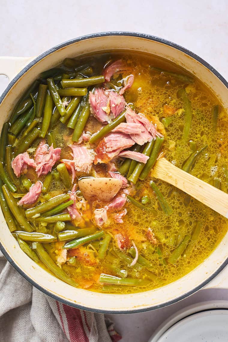 A large pot of string beans with ham hock being stirred