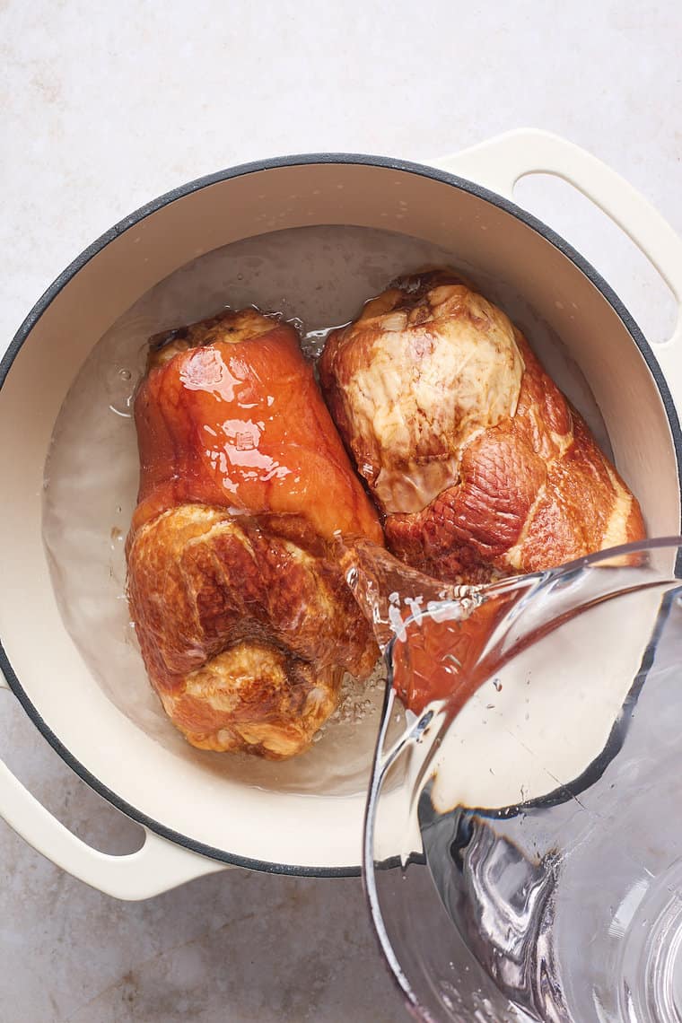 Water being poured on two ham hocks in a large pot