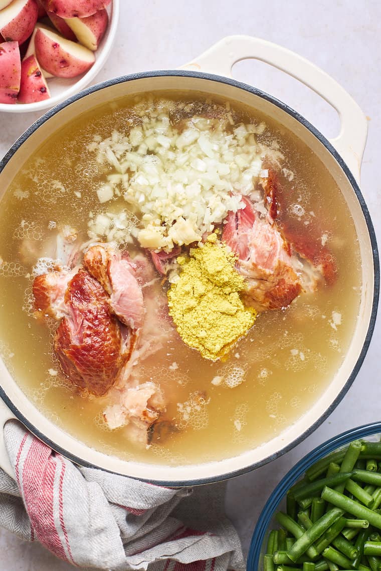 Spices and onions with ham hock in a large pot simmering