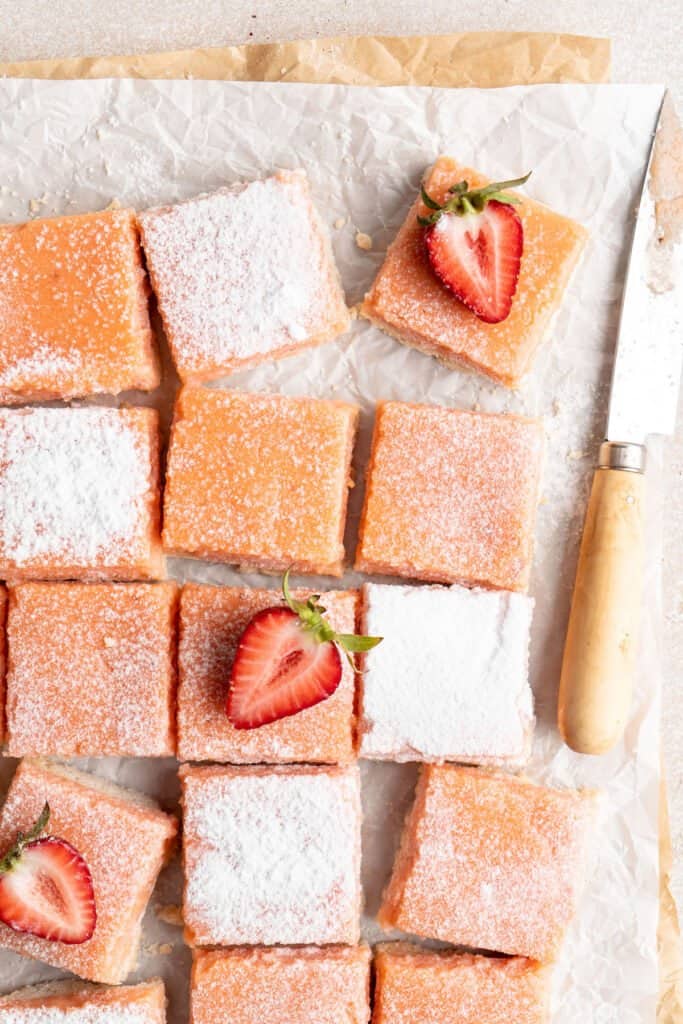 A close up of strawberry lemonade bars with powdered sugar and strawberries on top