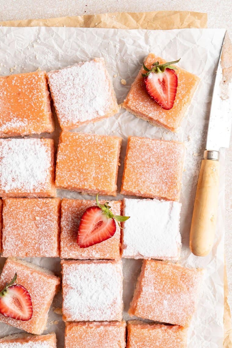 A close up of strawberry lemonade bars with powdered sugar and strawberries on top
