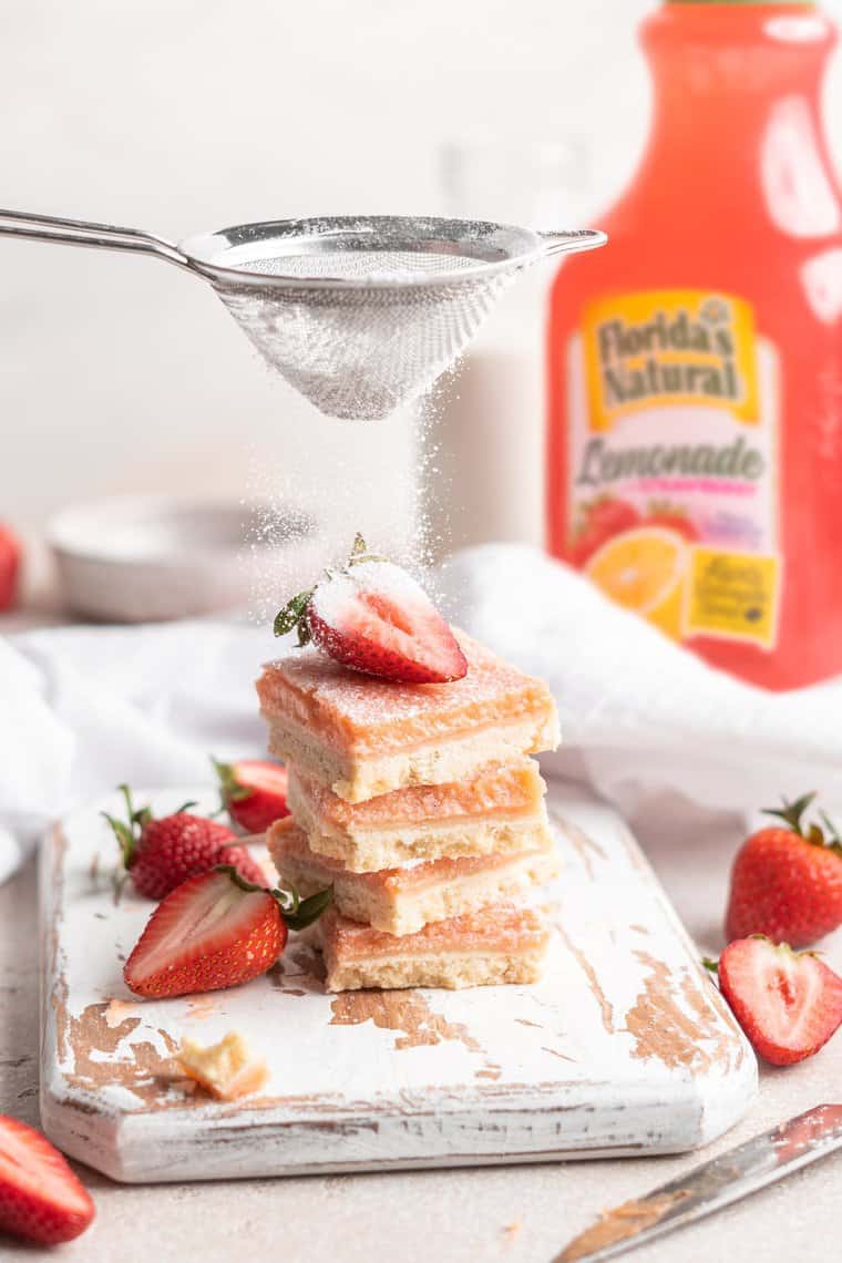 A stack of strawberry lemonade bars with powdered sugar being poured on top