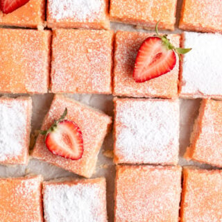 A close up of strawberry lemon bars with powdered sugar on top and strawberry slices