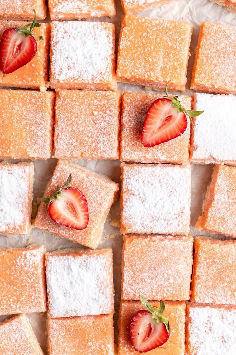 A close up of strawberry lemon bars with powdered sugar on top and strawberry slices