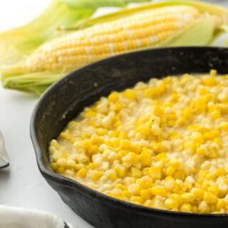 A skillet of fried corn only half shown in the image with an ear of fresh corn in the background.