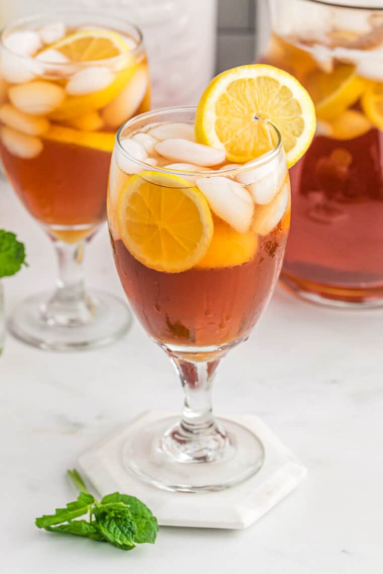 Two glasses of sweet tea recipe with a lemon wedge in one and a pitcher in the background.