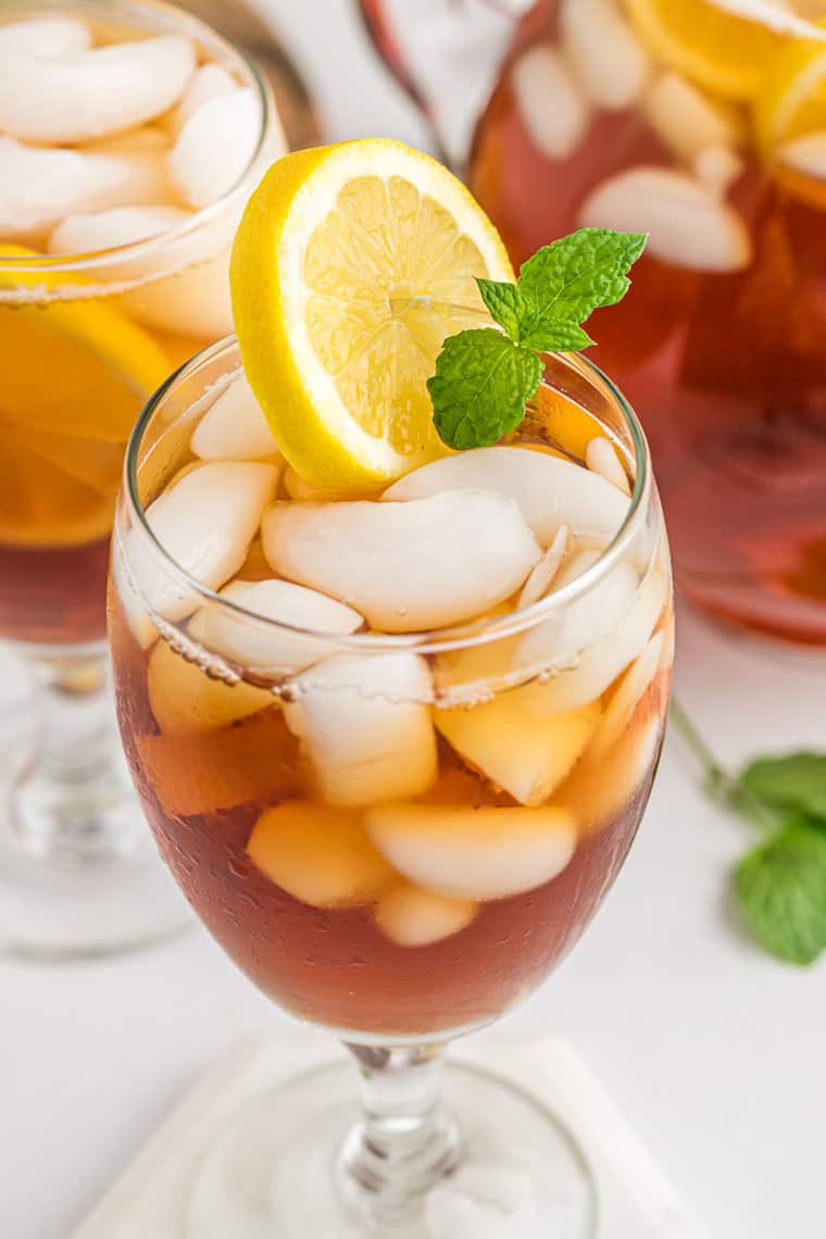 Two glasses of iced sweet tea with one in front with a lemon wedge and mint ready to serve.