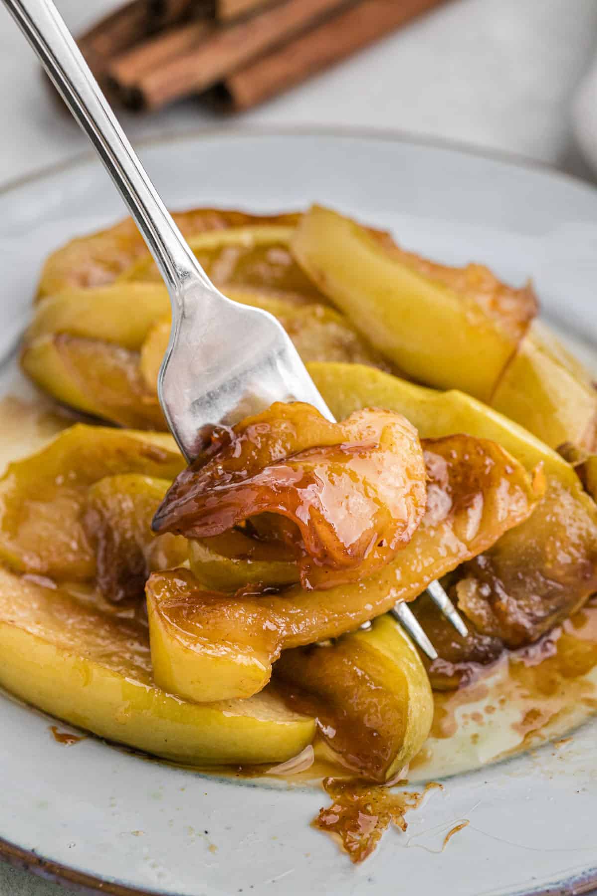 A Southern fried apple recipe on a white plate with a fork serving some up to eat