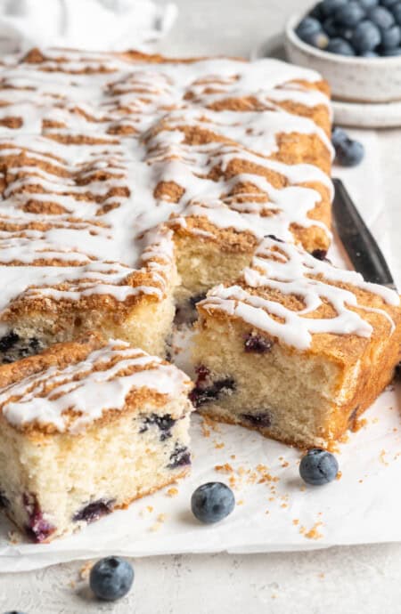 Slices of a blueberry coffee cake recipe ready to serve with fresh blueberries on parchment paper