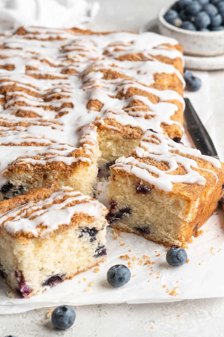 Slices of a blueberry coffee cake recipe ready to serve with fresh blueberries on parchment paper