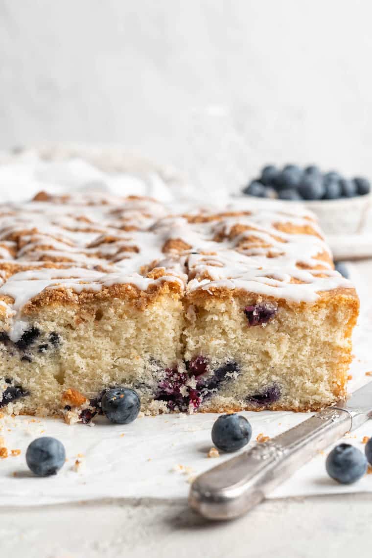 A close up of blueberry coffee cake ready to enjoy with a bowl of blueberries in the background
