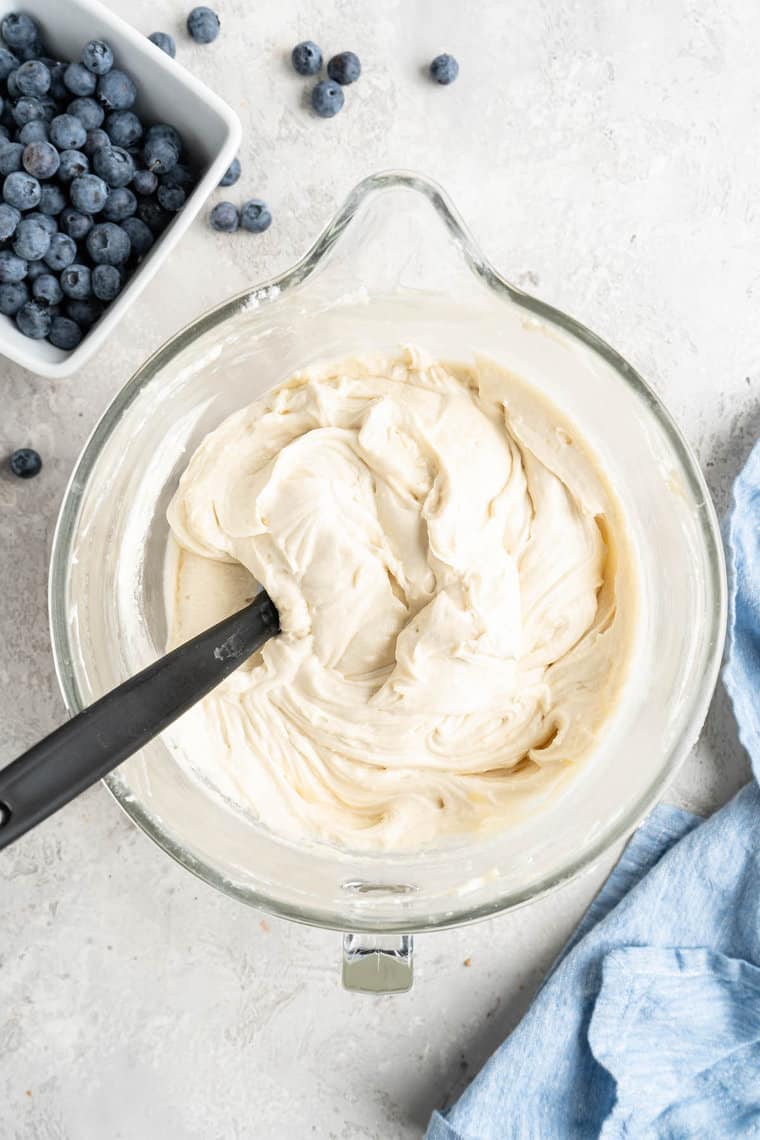 A cake batter in a mixing bowl with blueberries nearby